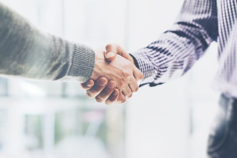Two men shake hands, only their arms and hands are visible.