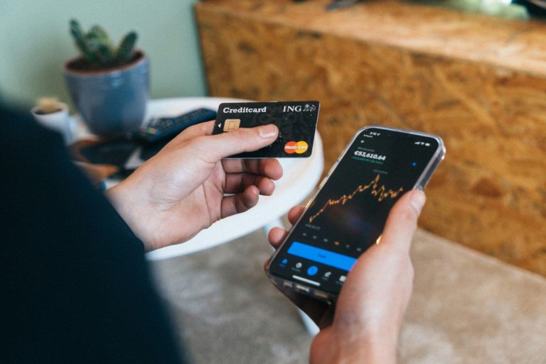 Mastercard debit card next to phone with price chart (CardMapr.nl/Unsplash)