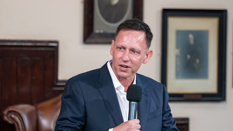 Peter Thiel holds a microphone while speaking at The Cambridge Union.
