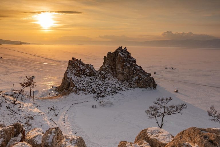 Wan sunlight shines on a two rock formations in a snow covered landscape.
