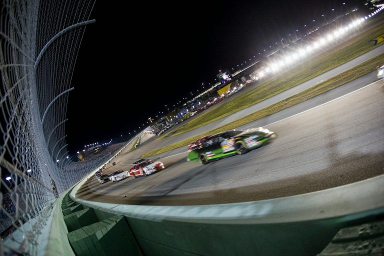 Cars speed round a racing track.