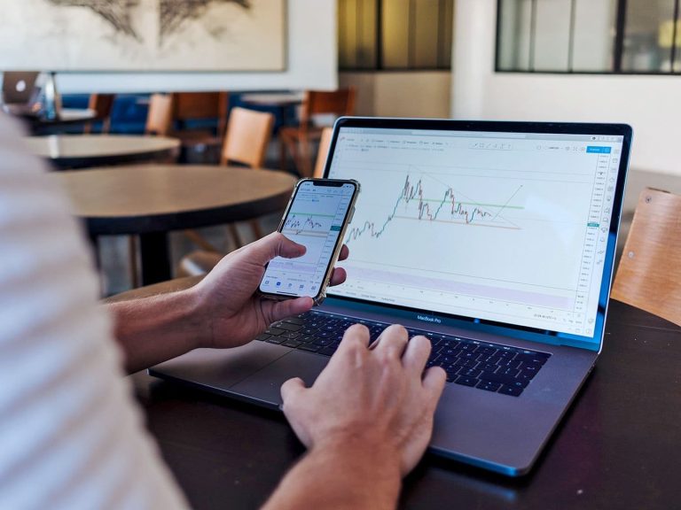 Man sitting at laptop computer holding smartphone checking charts