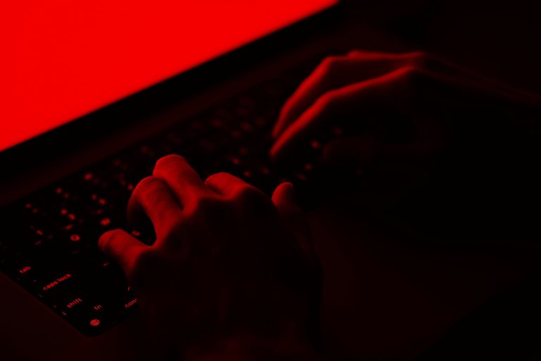 Under a low-light red lamp, a pair of hands types on a keyboard. (Wesley Tingey/Unsplash+)