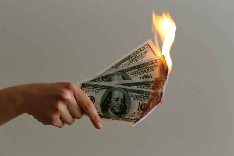 A hand holds dollar flaming bills (JP Valery/Unsplash)