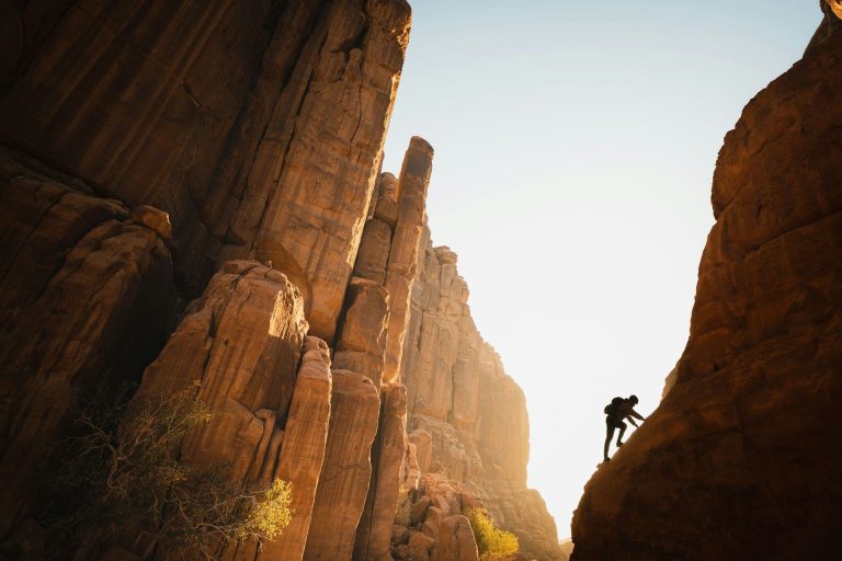 A rock climber silhouetted against the sky scales an incline in Saudi Arabia's Neom nature reserve.